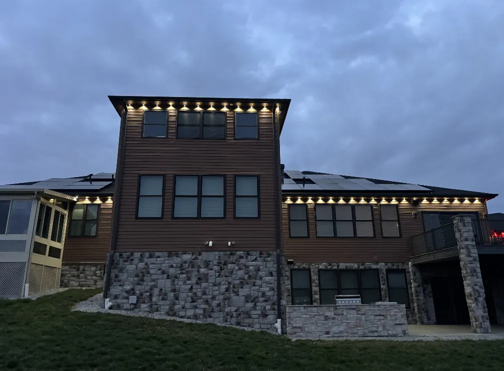 Rear of a two-story home with warm white permanent lights under the eaves at twilight